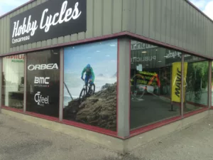 Photo extérieur de la vitrine d'un magasin de vélo "Hobby Cycles", surplombée de son enseigne.